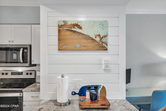 room details with ornamental molding, white cabinetry, light stone countertops, and appliances with stainless steel finishes