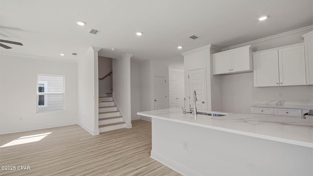 kitchen with light stone counters, a sink, visible vents, white cabinets, and ornamental molding