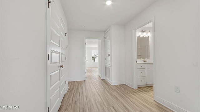 corridor featuring light wood-style flooring, baseboards, and a sink