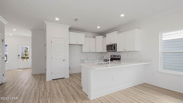 kitchen with visible vents, white cabinets, a peninsula, stainless steel appliances, and a sink