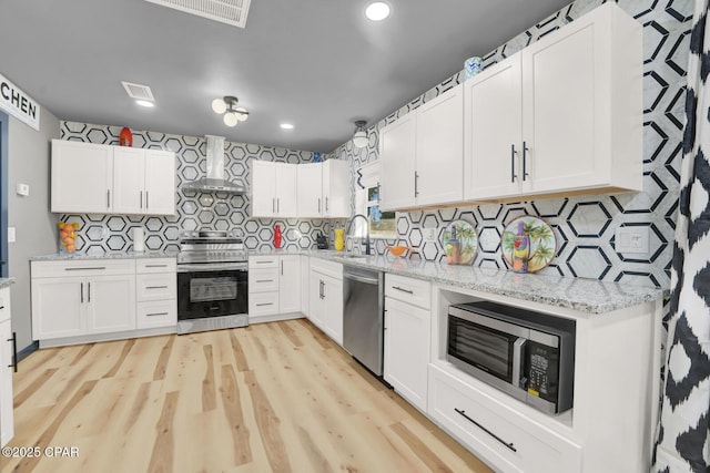 kitchen featuring sink, white cabinets, light stone counters, stainless steel appliances, and wall chimney exhaust hood