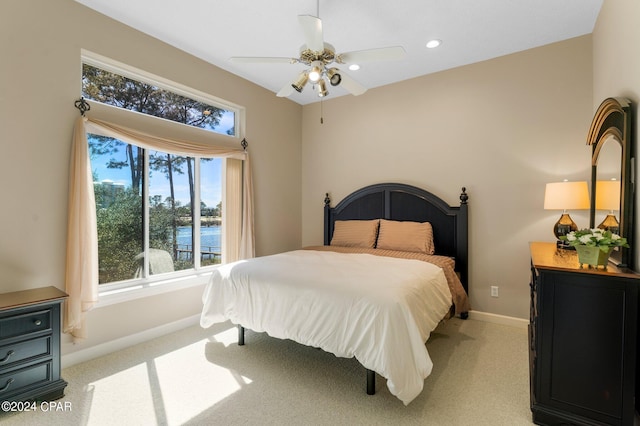 bedroom with light carpet, a water view, and ceiling fan