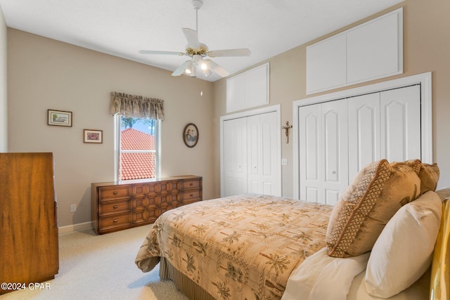 bedroom with ceiling fan, light colored carpet, and two closets