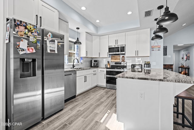 kitchen featuring sink, appliances with stainless steel finishes, dark stone countertops, hanging light fixtures, and white cabinets