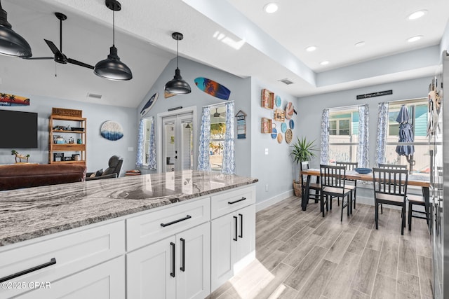 kitchen with pendant lighting, light stone countertops, white cabinets, french doors, and light wood-type flooring