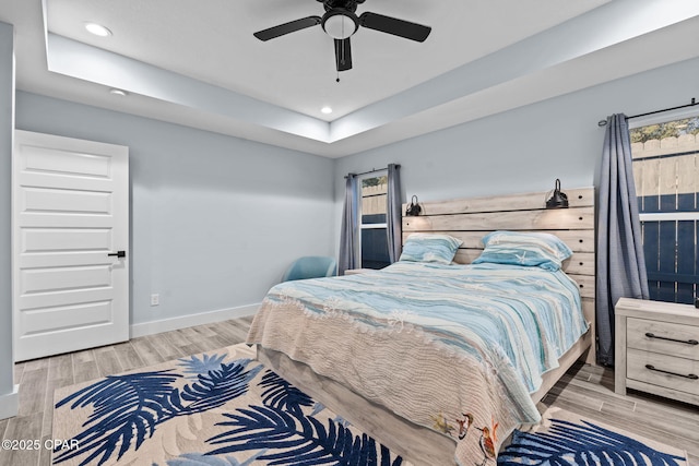 bedroom featuring ceiling fan, a tray ceiling, and light hardwood / wood-style floors