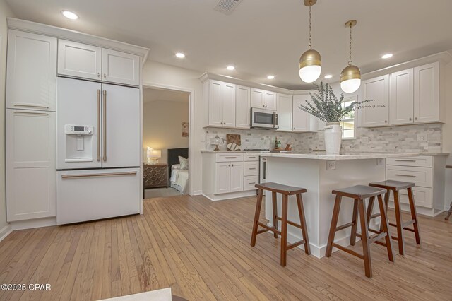 kitchen featuring hanging light fixtures, light hardwood / wood-style floors, white cabinets, decorative backsplash, and built in fridge