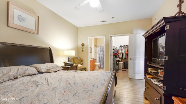 bedroom featuring connected bathroom, a walk in closet, light wood-type flooring, a closet, and ceiling fan