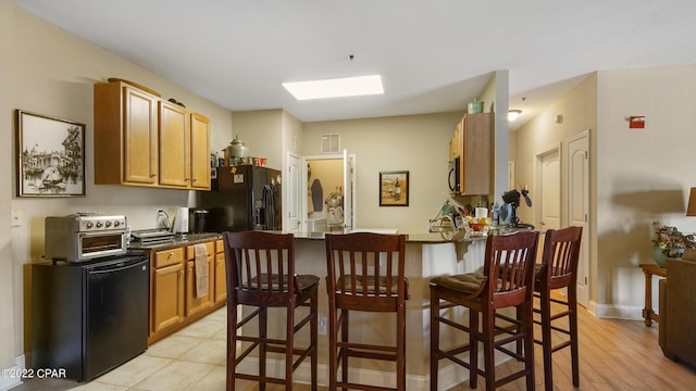 kitchen featuring black fridge, light tile patterned floors, a kitchen breakfast bar, and kitchen peninsula