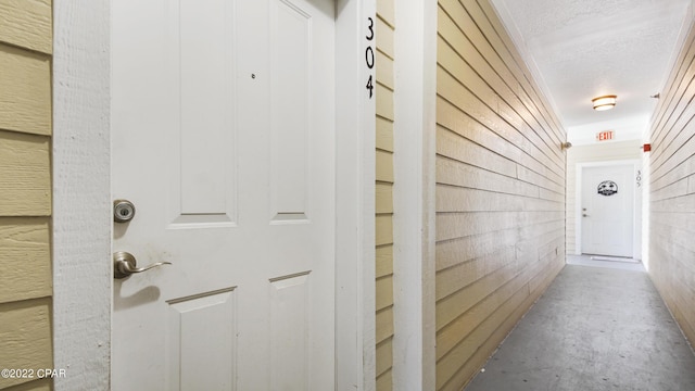 hallway with concrete floors, a textured ceiling, and wood walls