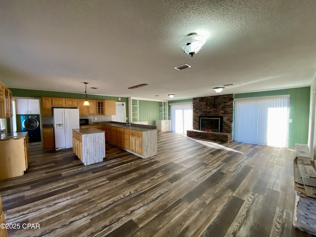 kitchen with dark wood-type flooring, washer / dryer, white refrigerator with ice dispenser, a kitchen island, and decorative light fixtures