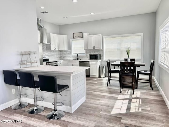 kitchen featuring a breakfast bar area, white cabinetry, kitchen peninsula, stainless steel appliances, and backsplash