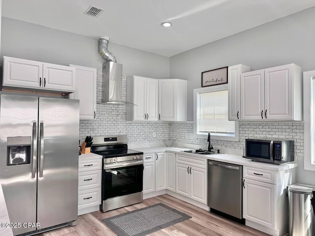 kitchen featuring wall chimney exhaust hood, sink, white cabinetry, light wood-type flooring, and stainless steel appliances