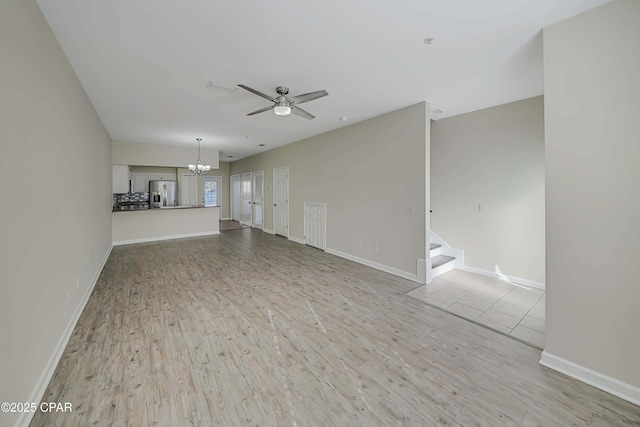 unfurnished living room featuring ceiling fan with notable chandelier and light wood-type flooring