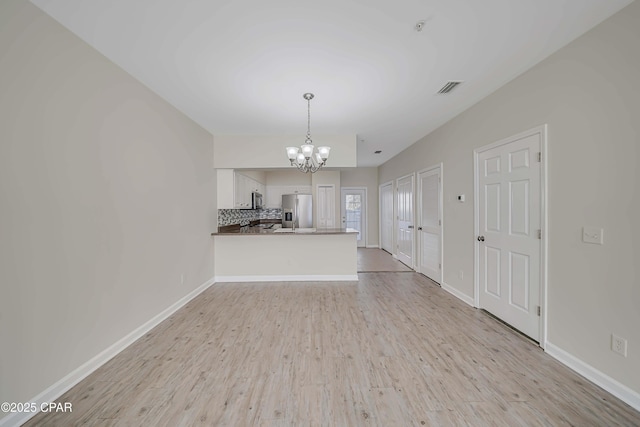 unfurnished living room with a notable chandelier and light hardwood / wood-style floors