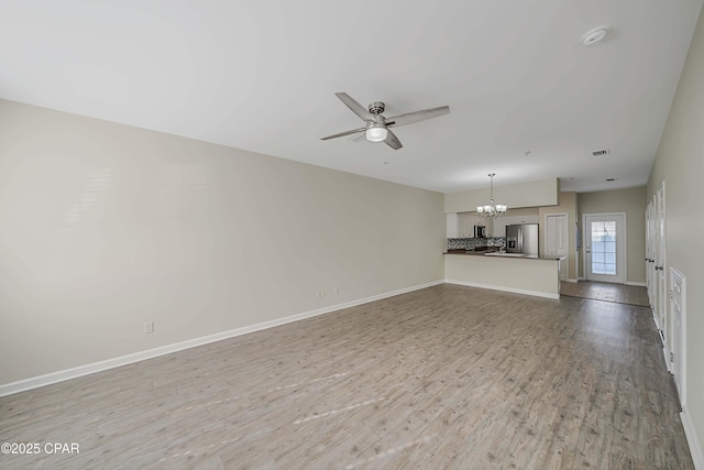 unfurnished living room with ceiling fan with notable chandelier and light hardwood / wood-style flooring