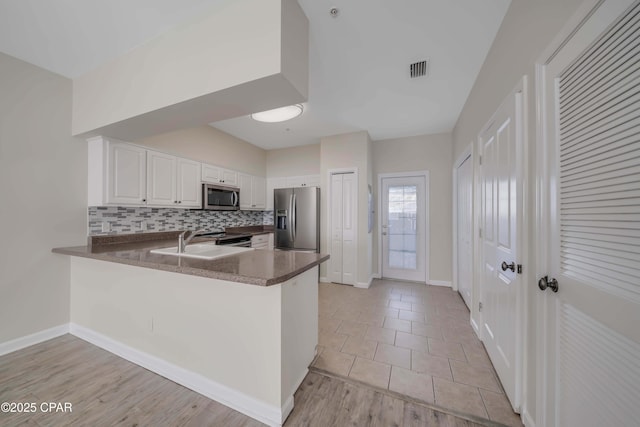 kitchen featuring white cabinetry, stainless steel appliances, kitchen peninsula, and decorative backsplash