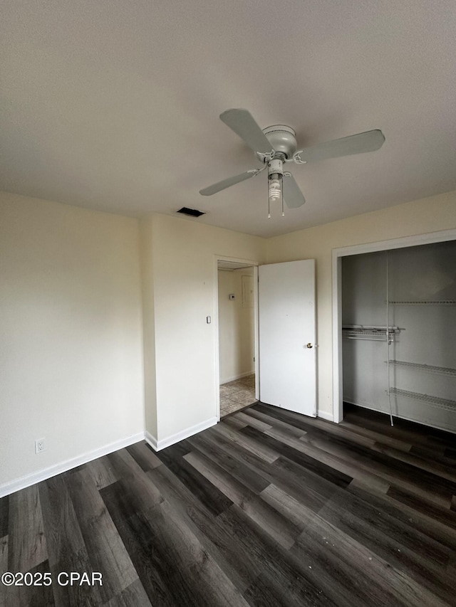 unfurnished bedroom with dark wood-style floors, a closet, visible vents, a ceiling fan, and baseboards