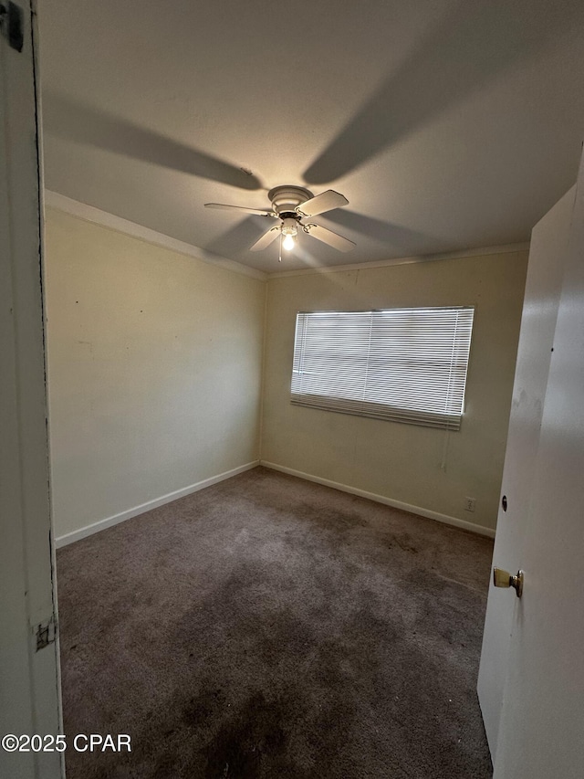 empty room featuring a ceiling fan, dark colored carpet, crown molding, and baseboards