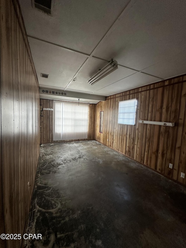 empty room with wood walls, unfinished concrete flooring, and visible vents