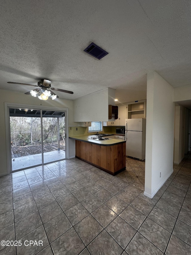 kitchen featuring visible vents, light countertops, freestanding refrigerator, built in microwave, and a peninsula