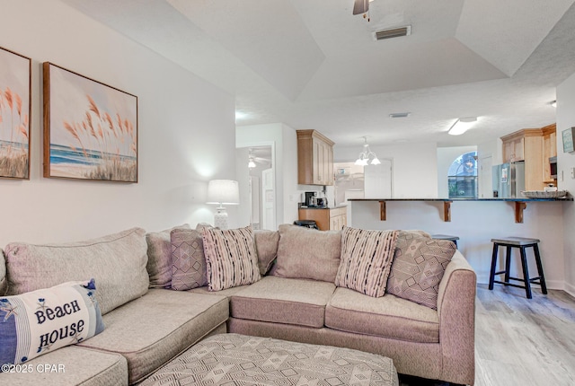 living area featuring a tray ceiling, visible vents, light wood finished floors, and ceiling fan