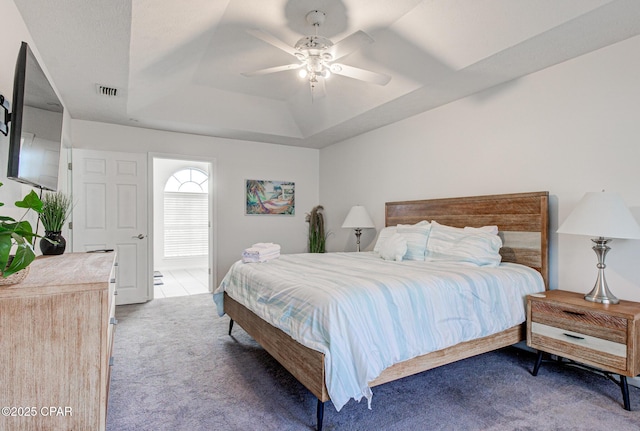 carpeted bedroom with visible vents, a raised ceiling, and a ceiling fan