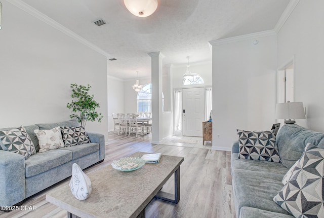 living room featuring light wood finished floors, visible vents, baseboards, ornamental molding, and a notable chandelier