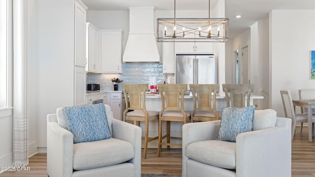 interior space featuring stainless steel refrigerator, white cabinets, custom exhaust hood, and pendant lighting