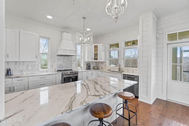 kitchen featuring sink, appliances with stainless steel finishes, white cabinetry, custom range hood, and a chandelier