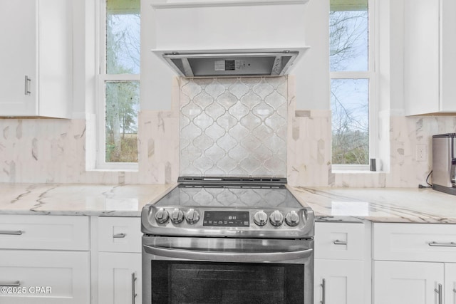 kitchen with light stone countertops, a healthy amount of sunlight, white cabinets, and stainless steel electric range