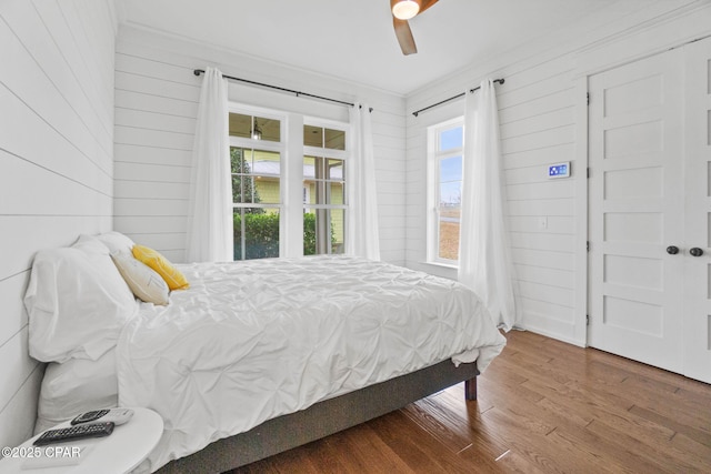 bedroom with hardwood / wood-style flooring, crown molding, ceiling fan, and wood walls