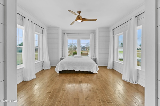 bedroom with ceiling fan, ornamental molding, wooden walls, and light hardwood / wood-style flooring