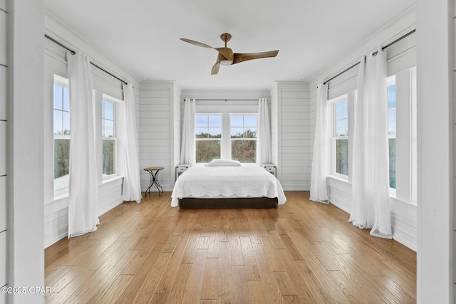 bedroom with light wood-type flooring, ornamental molding, ceiling fan, and wood walls