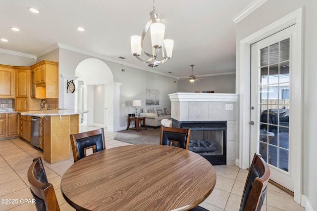 dining room featuring decorative columns, a tiled fireplace, ornamental molding, light tile patterned floors, and ceiling fan