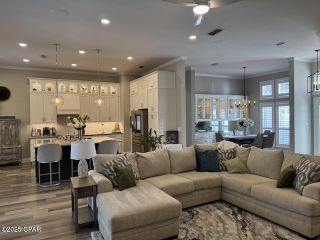 living room featuring ornamental molding, wood-type flooring, and ceiling fan with notable chandelier