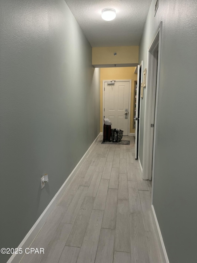 hall featuring baseboards, light wood-style floors, and a textured ceiling