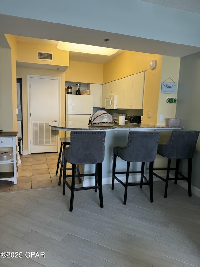 kitchen featuring white appliances, visible vents, a peninsula, white cabinetry, and dark countertops