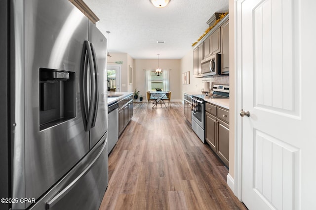 kitchen with decorative light fixtures, a textured ceiling, dark hardwood / wood-style flooring, stainless steel appliances, and backsplash