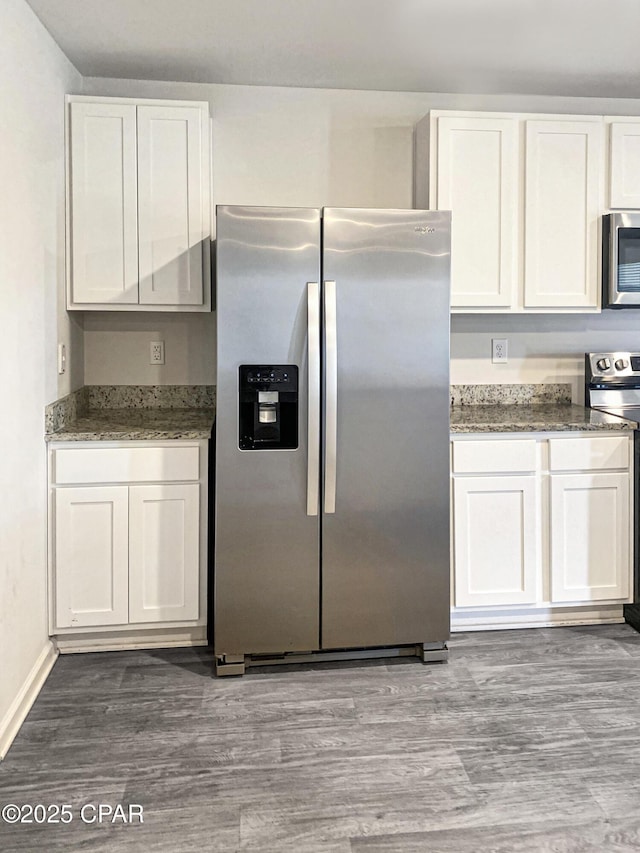 kitchen featuring white cabinetry, wood-type flooring, dark stone countertops, and appliances with stainless steel finishes