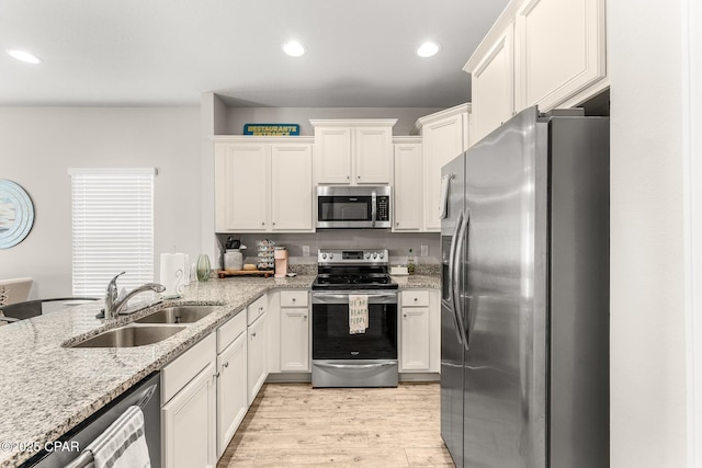 kitchen featuring sink, white cabinetry, light wood-type flooring, stainless steel appliances, and light stone countertops