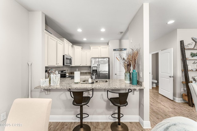 kitchen with light stone counters, white cabinetry, a kitchen breakfast bar, kitchen peninsula, and stainless steel appliances