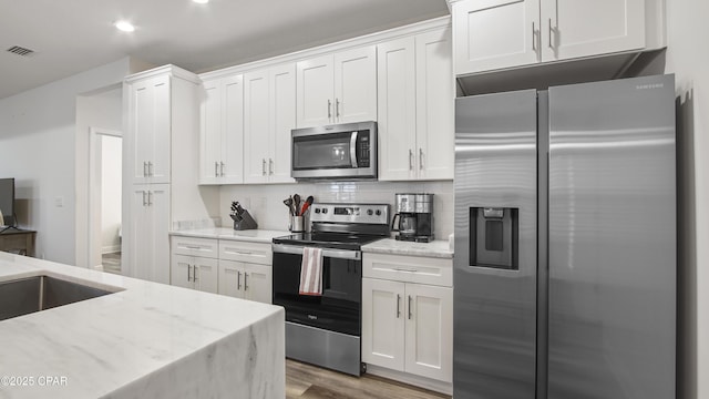 kitchen with appliances with stainless steel finishes, light stone countertops, hardwood / wood-style floors, and white cabinets