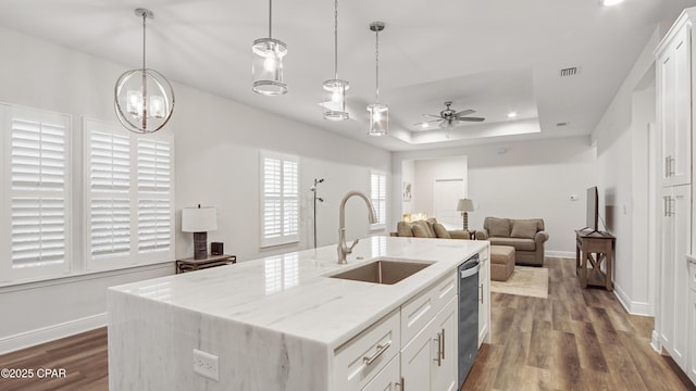 kitchen featuring white cabinetry, an island with sink, a tray ceiling, and sink