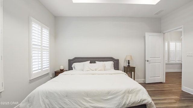 bedroom with multiple windows, a skylight, and dark hardwood / wood-style floors