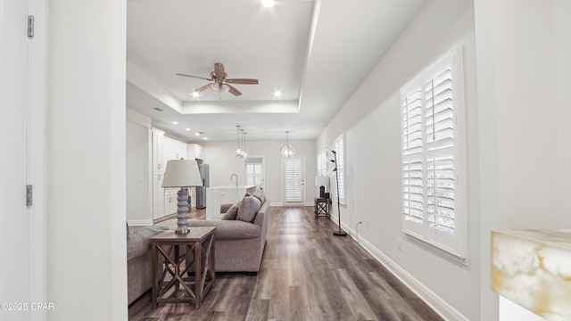 living room with ceiling fan with notable chandelier, dark hardwood / wood-style flooring, and a tray ceiling