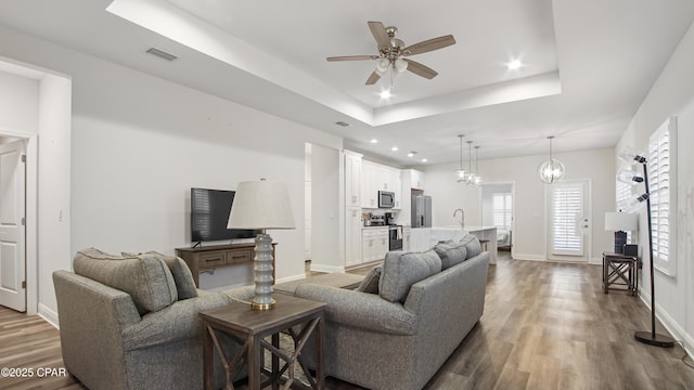 living room featuring dark hardwood / wood-style floors, ceiling fan, and a tray ceiling