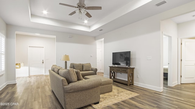 living room with ceiling fan, wood-type flooring, and a tray ceiling