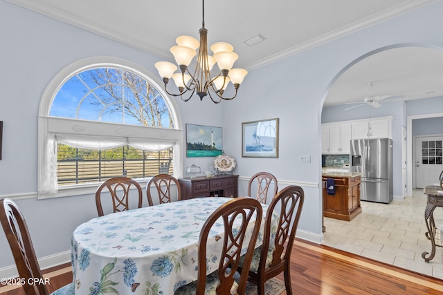 dining room with arched walkways, light wood finished floors, visible vents, ornamental molding, and ceiling fan with notable chandelier