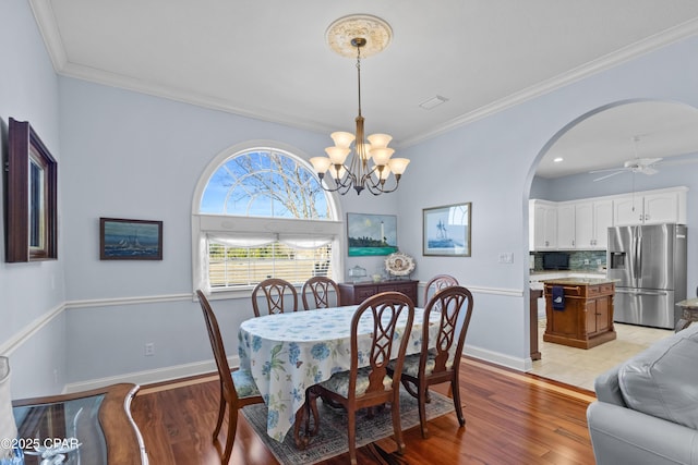 dining room featuring light wood finished floors, baseboards, arched walkways, and crown molding